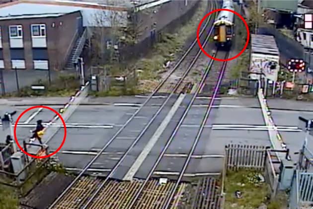Man climbs train crossing barrier and strolls across tracks moments before a high speed train travels through at Station Road in Langley Green, Oldbury, West Midlands, on April 27, 2024.