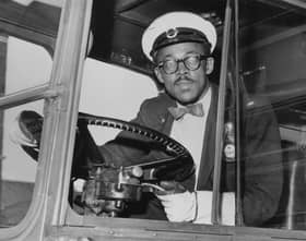 A bus driver at the wheel, wearing a checked bow tie, in around 1965