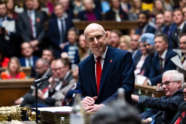 A photograph of John Healey stood at the dispatch box of the House of Commons with MPs behind him
