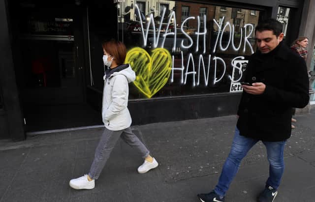 People pass graffiti reminding people to wash their hands on the window of a bar in Dublin's city centre, on the first day of a series of sweeping virus delay measures in Ireland, including school closures. Picture: Brian Lawless/PA Wire