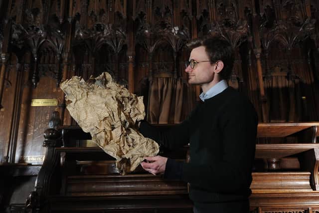Tristram Bainbridge pictured with a copy of the Leeds Mercury dated 1868 from behind the Fallen Angel at Ripon Cathedrall. Image: Simon Hulme