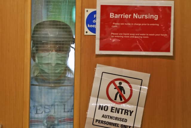 A nurse wearing PPE looks through a hospital window