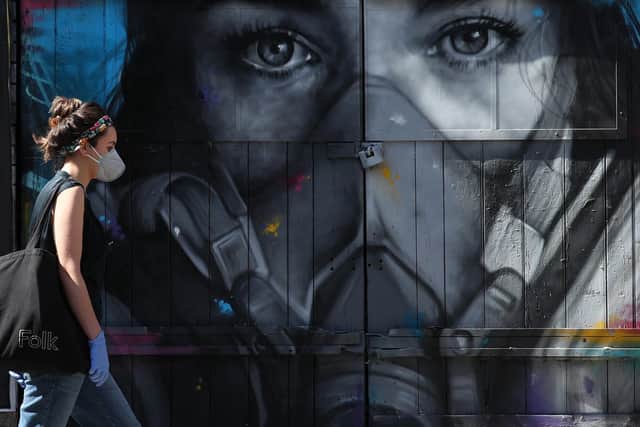 A woman wearing a face mask walking past a piece of street art entitled s(P)ray, by French street artist Zabou, as the UK continues in lockdown to help curb the spread of the coronavirus. Photo: PA