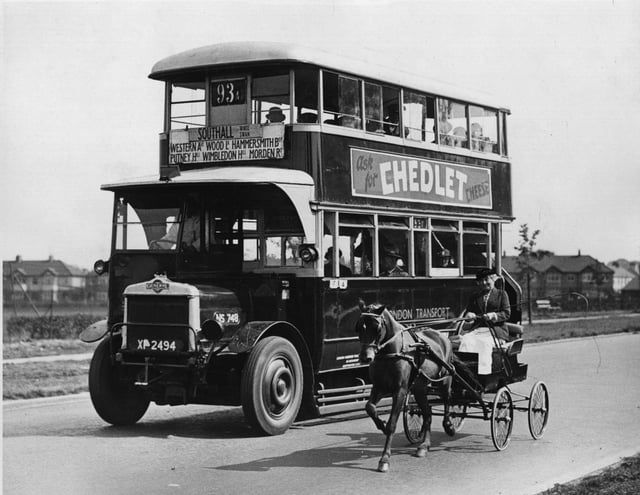 circa 1920:  A woman with a very small open horse-drawn carriage rides alongside a bus bound for Southall.  (Photo by Fox Photos/Getty Images)