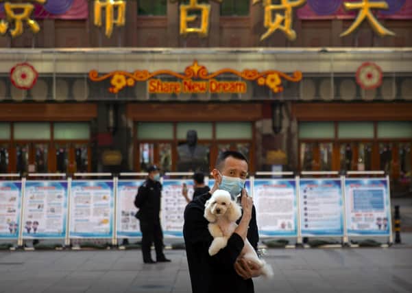 A man wearing a face mask to prevent the spread of the new coronavirus holds a dog as he stands along a pedestrian shopping street in Beijing as calls are made to reset UK relations with China.