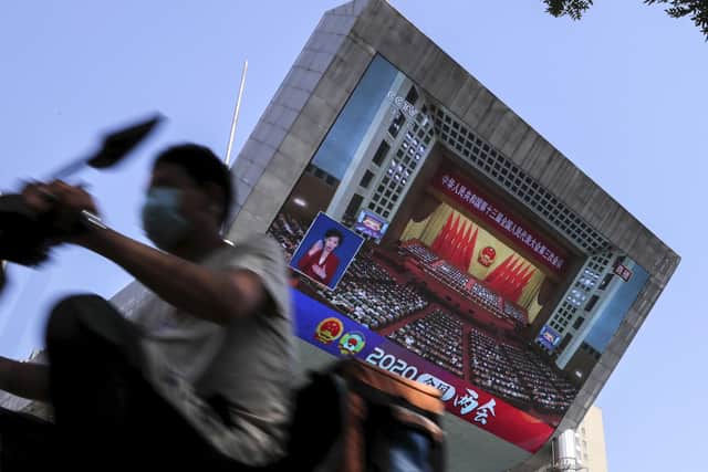 A food delivery worker wearing a face mask to protect against the spread of the new coronavirus passes by a TV screen showing the closing ceremony of the National People's Congress in a news report, in Beijing. . China's ceremonial legislature endorsed a national security law for Hong Kong that has strained relations with the United States and Britain.