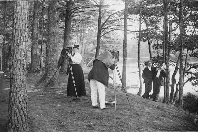 A woman adjusts her camera as a man takes a photo of two men in the woods, early 1900s. (Photo by Hulton Archive/Getty Images)