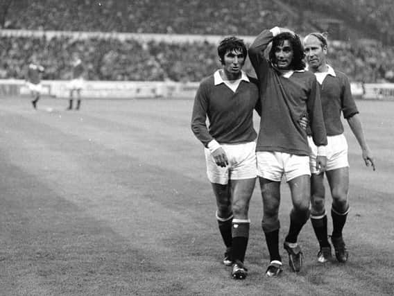 An unbelieving George Best, the Manchester United and Irish International, is helped off the field by teammates (on the right) Bobby Charlton and (on the left) Tony Dunne during a match against Chelsea at Stamford Bridge in 1971. (Photo by Central Press/Getty Images)