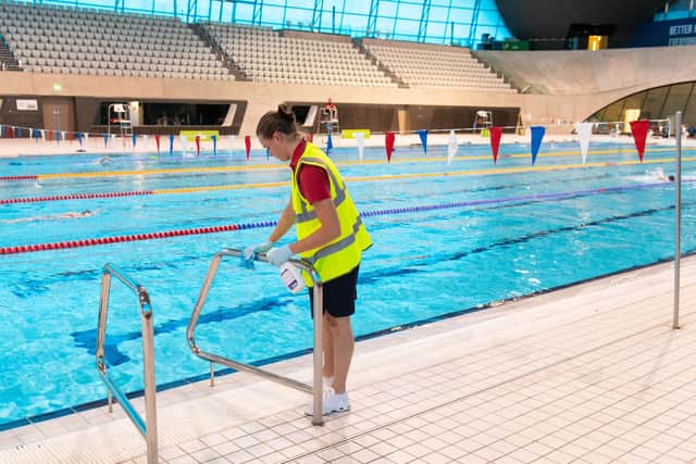Keeping safe: A member of staff cleans poolside railings at the London Aquatic Centre. Picture: PA