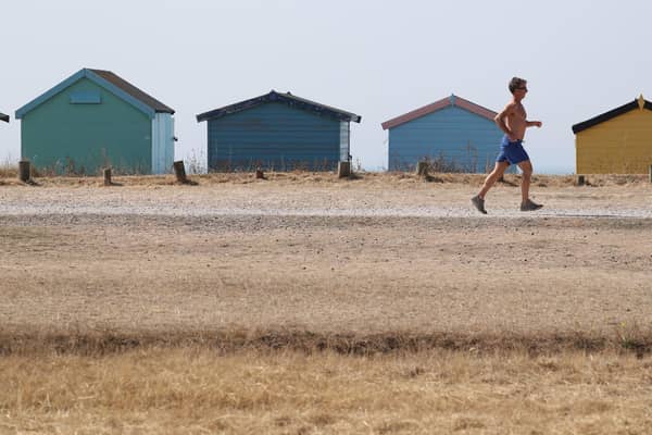 A runner jogs past beach huts as temperatures remain in the mid-30s.