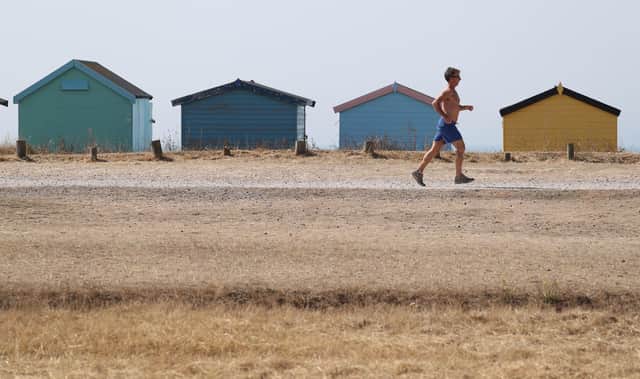 A runner jogs past beach huts as temperatures remain in the mid-30s.