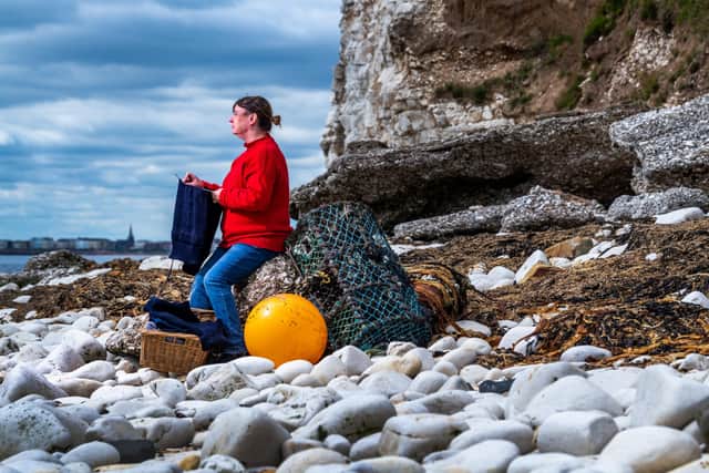 Donna Blyth, wearing and holding a half finished knitted traditional gansey, on the shore of South Landing at Flamborough. By James Hardisty.