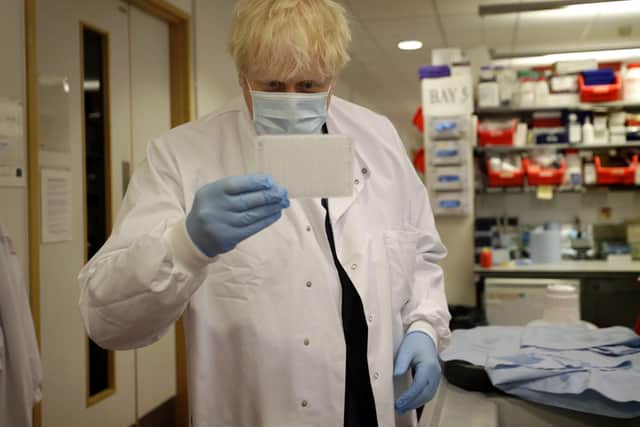 Prime Minister Boris Johnson looks at an immunological assay as he washes them during a visit to the Jenner Institute in Oxford, where toured the laboratory and met scientists leading Covid research.