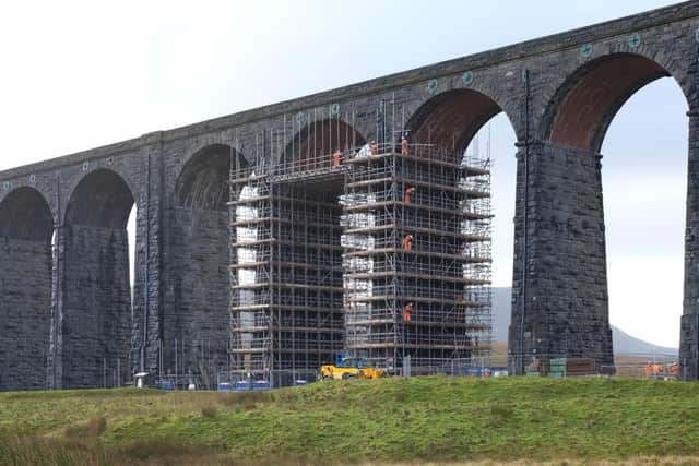 A column of construction workers haul scaffolding poles at Ribblehead Viaduct