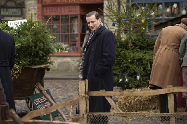 In this sneak preview from the All Creatures Great and Small Christmas special, James Herriot (Nicholas Ralph) soaks up Darrowby square's festive atmosphere wrapped up sensibly in a navy overcoat and fairisle knitted scarf.