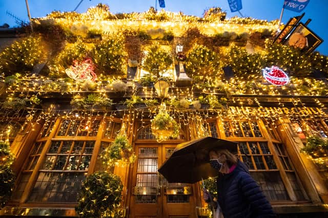 A woman in a face mask walks past Christmas lights outside a closed pub