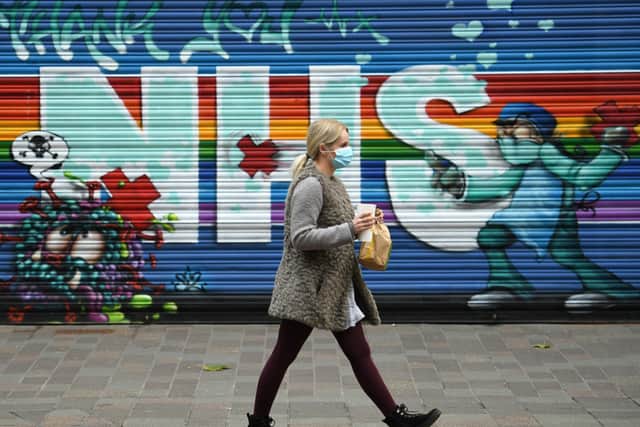 A pedestrian wearing a face mask walks past a mural praising the NHS.