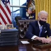 President Joe Biden reaches for a pen to sign his first executive order in the Oval Office.