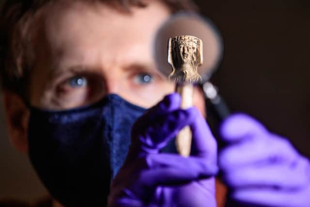 Andrew Woods, senior curator at the Yorkshire Museum, holds a magnifying glass in front of a medieval bone handle carving of a woman dressed in a gown and headdress, dating to the 14th Century