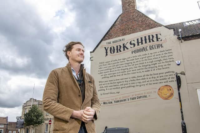 Tom Naylor-Leyland, who is the organiser of the Malton Food Festival, in front of the large mural of a Yorkshire pudding recipe dating from the 18th century which was created a couple of years ago on the side of McClaren's solicitors on Newgate