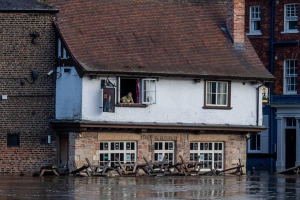 Colin Fidler, Landlord of the Kings Arms, King's Staith, York, peers from his upstairs window as rising floodwater from the River Ouse is pumped out of his pub Credit: James Hardisty