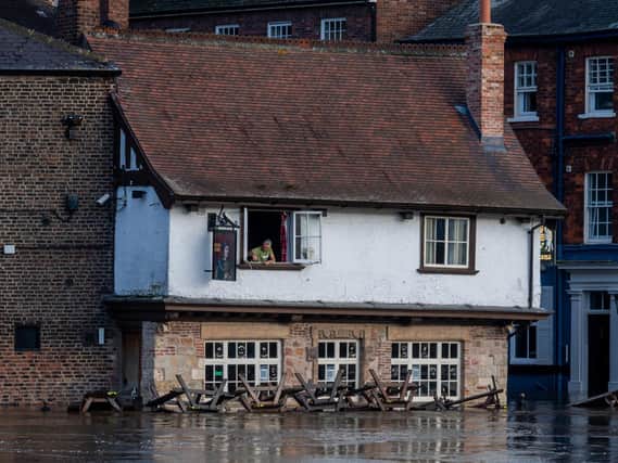 Colin Fidler, Landlord of the Kings Arms, King's Staith, York, peers from his upstairs window as rising floodwater from the River Ouse is pumped out of his pub Credit: James Hardisty
