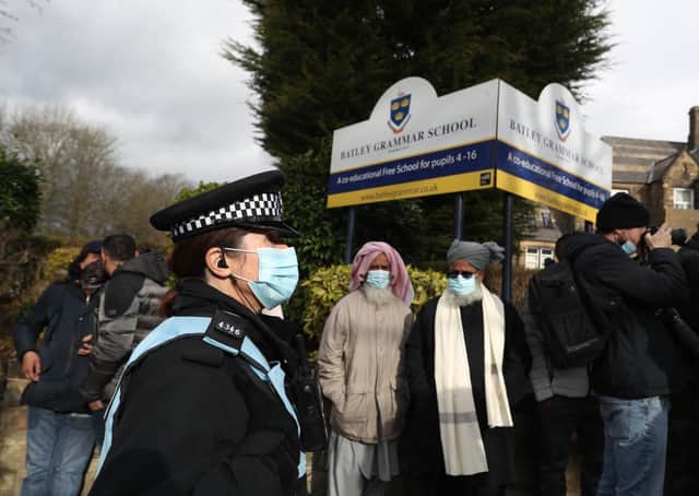 A police officer observes protesters gathered outside Batley Grammar School in Batley, West Yorkshire, where a teacher has been suspended for reportedly showing a caricature of the Prophet Mohammed to pupils during a religious studies lesson.