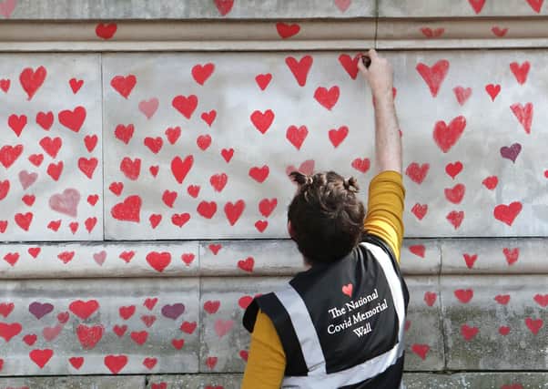 A volunteer paints hearts on the National Covid Memorial Wall on the Embankment, central London, which is being painted in memory of all those who have died from Covid.