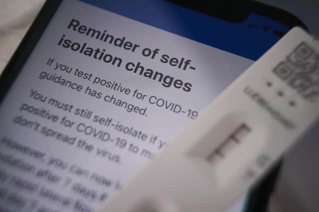 A positive lateral flow test cassette placed next to advice from the NHS COVID app on an iPhone, in London