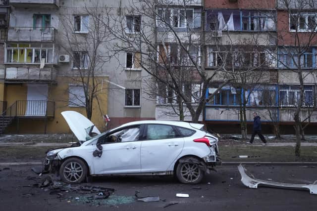 A man walks past a damaged vehicle and debris following Russian shelling in Mariupol, Ukraine.