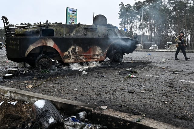 Armed man walks past a burned military vehicle on a check-point in the city of Brovary outside Kyiv on March 1, 2022.