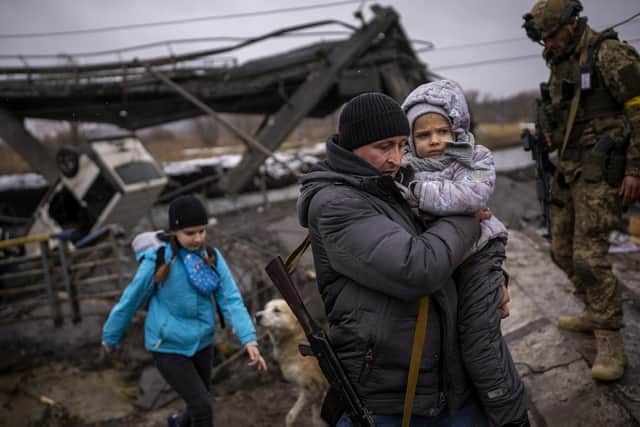 Local militiaman Valery, 37, carries a child as he helps a fleeing family across a bridge destroyed by artillery, on the outskirts of Kyiv, Ukraine, Wednesday, March 2. 2022. (AP Photo/Emilio Morenatti)