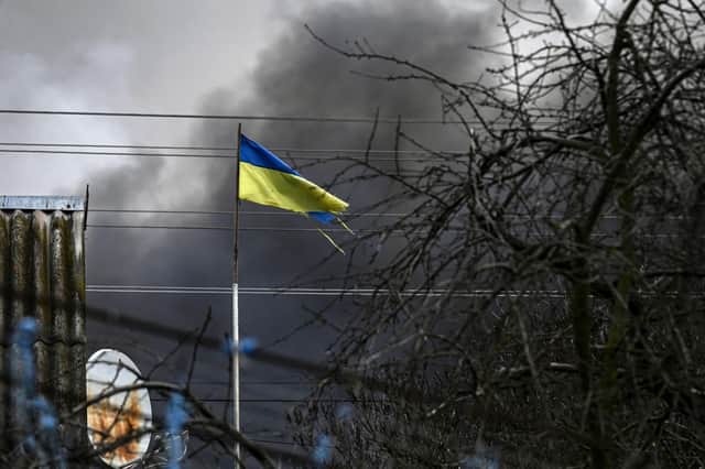 An Ukrainian flag waves in front of smoke rising from a bombed warehouse in the town of Stoyanka, west of Kyiv, on March 4, 2022. Photo by ARIS MESSINIS/AFP via Getty Images.