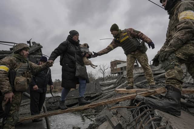 Ukrainian servicemen help a woman carrying a small dog cross the Irpin river on an improvised path under a bridge, that was destroyed by Ukrainian troops designed to slow any Russian military advance, while assisting people fleeing the town of Irpin, Ukraine, Saturday, March 5, 2022. What looked like a breakthrough cease-fire to evacuate residents from two cities in Ukraine quickly fell apart Saturday as Ukrainian officials said shelling had halted the work to remove civilians hours after Russia announced the deal. (AP Photo/Vadim Ghirda).