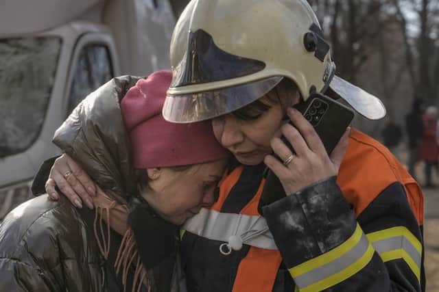 A firefighter comforts a woman outside a destroyed apartment building after a bombing in a residential area in Kyiv, Ukraine, Tuesday, March 15, 2022.