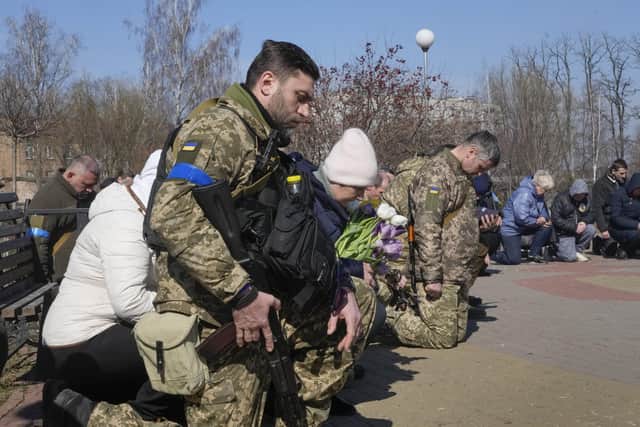 Ukrainian soldiers and civilians stand kneeling as they pay their last tribute to colonel Valeriy Gudz who was killed in a battle against Russians, at a cemetery in the town of Boryspil close to capital Kyiv, Ukraine, Tuesday, March 15, 2022. Russian forces are pounding Ukrainian cities and edging closer to the capital, Kyiv, in a relentless bombardment that keeps deepening the war's humanitarian crisis. (AP Photo/Efrem Lukatsky).