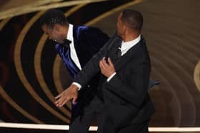 presenter Chris Rock, left, reacts after being hit on stage by Will Smith while presenting the award for best documentary feature at the Oscars on Sunday, March 27, 2022, at the Dolby Theatre in Los Angeles.