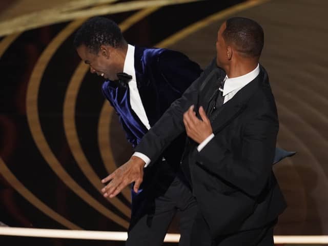 presenter Chris Rock, left, reacts after being hit on stage by Will Smith while presenting the award for best documentary feature at the Oscars on Sunday, March 27, 2022, at the Dolby Theatre in Los Angeles.