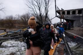 A woman carries her pet cat as evacuees cross a destroyed bridge as they flee the city of Irpin, northwest of Kyiv, on March 7, 2022. Photo by Dimitar DILKOFF / AFP via Getty Images.
