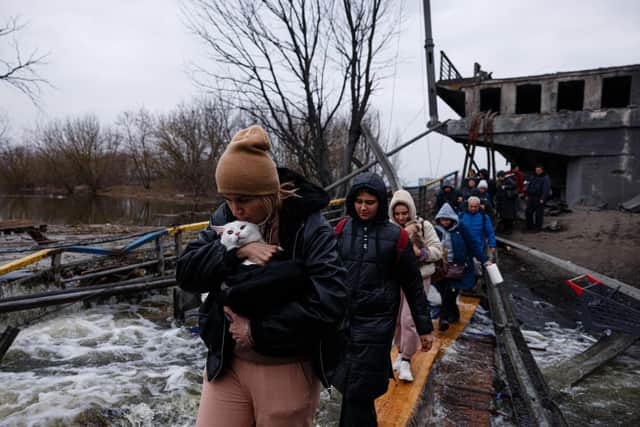 A woman carries her pet cat as evacuees cross a destroyed bridge as they flee the city of Irpin, northwest of Kyiv, on March 7, 2022. Photo by Dimitar DILKOFF / AFP via Getty Images.