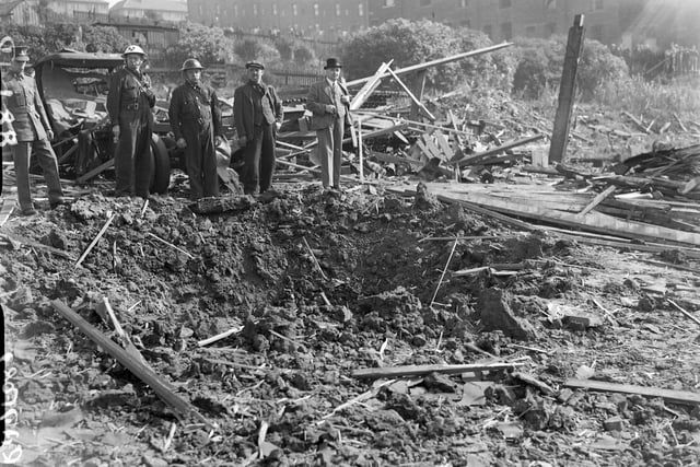 Bomb damage in Bradford showing a bomb crater with wrecked vehicle. Pictured are ARPs and officer in uniform as well as civilians. Taken in 1940.