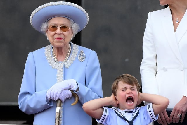 Prince Louis of Cambridge holds his ears as he stands next to Queen Elizabeth II to watch a special flypast from the Buckingham Palace balcony.