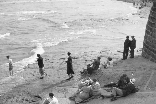 A group of people watching the sea from the dock at Robin Hood's Bay. (Photo by Alfred Hind Robinson/A H Robinson/Hulton Archive/Getty Images)