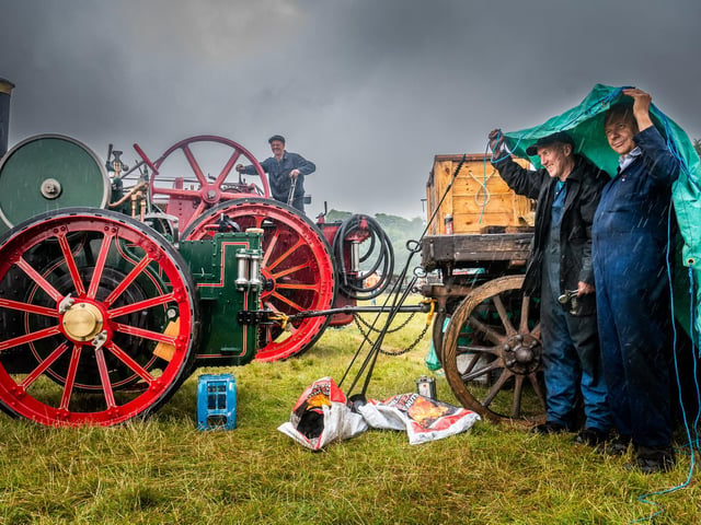 John Appleby, of Pickering, works on Old Lass, a 1901 7 horsepower agricultural Traction Engine, whilst Mark Angusm and Rod Lytton, shelter from a heavy rain shower.