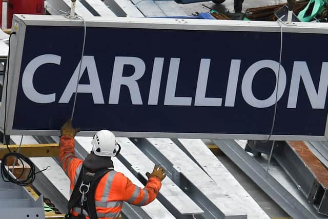 A worker guides down a sign showing the name of liquidated British construction and outsourcing group Carillion after it was taken down off a construction crane on a building site in the City of London on January 23, 2018. (Photo credit should read DANIEL SORABJI/AFP/Getty Images.