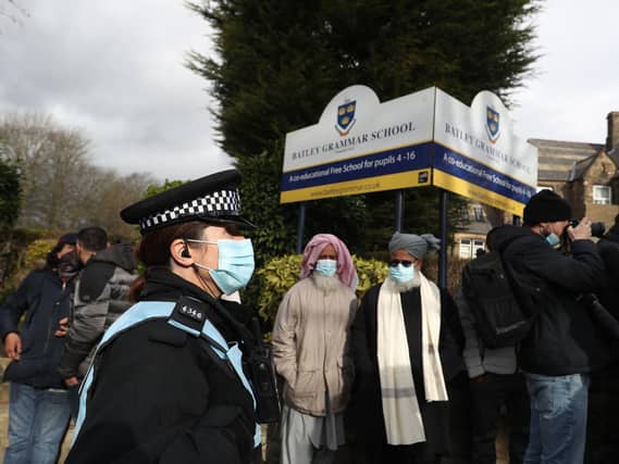A police officer observes protesters gathered outside Batley Grammar School in Batley, West Yorkshire, where a teacher was suspended for reportedly showing a caricature of the Prophet Mohammed to pupils during a religious studies lesson in March. Photo credit: Danny Lawson/PA Wire