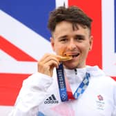 Tom Pidcock of Team Great Britain bites his gold medal and pose with the flag of his country in the background after the Men's Cross-country race on day three of the Tokyo 2020 Olympic Games at Izu Mountain Bike Course on July 26, 2021 in Izu, Shizuoka, Japan. (Picture: Michael Steele/Getty Images)