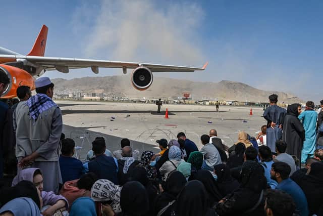 Afghan people sit along the tarmac as they wait to leave the Kabul airport in Kabul on August 16, 2021, after a stunningly swift end to Afghanistan's 20-year war, as thousands of people mobbed the city's airport trying to flee the group's feared hardline brand of Islamist rule. (Photo by Wakil Kohsar / AFP) (Photo by WAKIL KOHSAR/AFP via Getty Images).