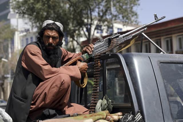 A Taliban fighter sits on the back of vehicle with a machine gun in front of the main gate leading to the Afghan presidential palace, in Kabul, Afghanistan.