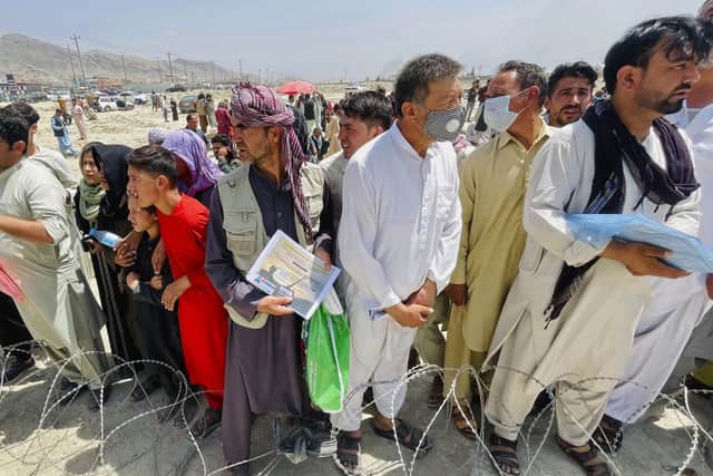 A man holds a certificate acknowledging his work for Americans as hundreds of people gather outside the international airport in Kabul, Afghanistan, as the humanitarian crisis deepens.